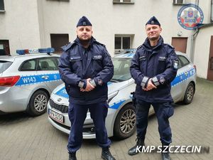 dwaj policjanci stoją przed radiowozem policyjnym