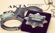 odznaka policyjna i kajdanki leżą na teczce z aktami sprawy