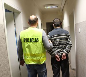 umundurowany policjant prowadzi korytarzem podejrzanego