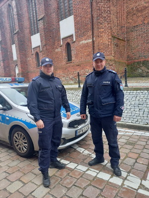 dwaj policjanci stoją przed radiowozem