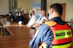 Sześć osób, w tym dwoje policjantów w mundurach, siedzi za stołami na spotkaniu z Zastępcą Prezydenta Gdańska