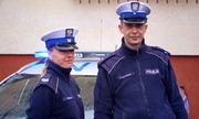 policjant i policjantka stoją przy radiowozie