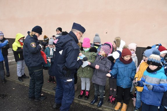 Policjant i funkcjonariuszka Straży Miejskiej rozdają ulotki informacyjne grupie dzieci.