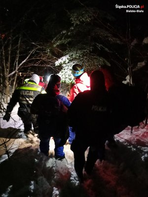 Ratownicy i Policjanci po śniegu w lesie prowadzą nosze z poszkodowanym. Zdjęci wykonane w nocy zimą