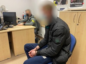 zatrzymany mężczyzna siedzi na krześle przed biurkiem policjanta, na ręce ma założone kajdanki