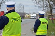 dwóch policjantów ruchu drogowego w żółtych kamizelkach z napisem Policja na plecach stoi przy drodze