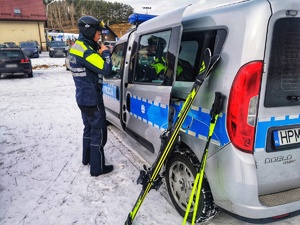 policjant stoi przy radiowozie policyjnym, obok stoją narty oparte o samochód