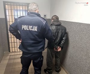 policjant prowadzi do celi skutego kajdankami zatrzymanego