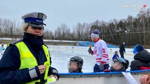 policjantka prezentująca element odblaskowy. w tle odbywa się trening hokeja na lodowisku