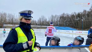 policjantka prezentująca element odblaskowy. w tle odbywa się trening hokeja na lodowisku