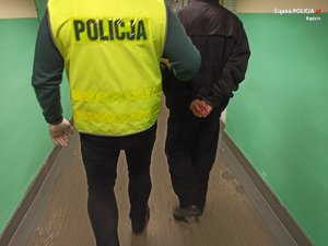 policjant prowadzi zatrzymanego mężczyznę w kajdankach