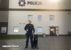 policjant stoi z psem służbowym przed budynkiem komendy policji