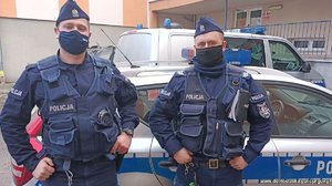dwóch umundurowanych policjantów stoi przed radiowozem