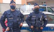 dwóch umundurowanych policjantów stoi przed radiowozem