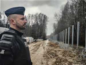 policjant stoi naprzeciwko budowanej zapory granicznej
