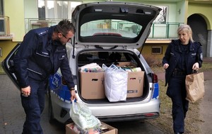 dwoje umundurowanych policjantów wypakowuje z radiowozu dary zebrane dla potrzebującej kobiety