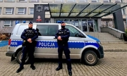 umundurowani policjanci stoją przy radiowozie, w tle budynek Policji