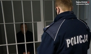 policjant stoi przy drzwiach z kraty, za którymi siedzi podejrzany