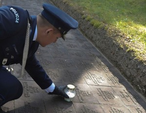 policjant składa hołd i  zapala świeczkę