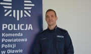 policjant stoi przy ściance Komendy Powiatowej Policji w Oławie