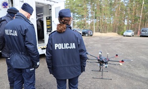 dwoje policjantów przed Mobilną Platformą Kryminalistyczną patrzy na stojącego drona