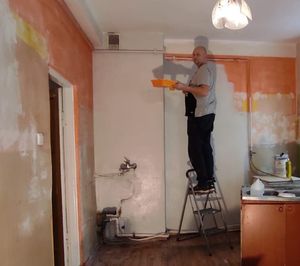 Mężczyzna na drabinie maluje ścianę w pokoju.&quot;&gt;