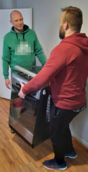 Dwóch mężczyzn wnosi kuchenkę gazową do pomieszczenia