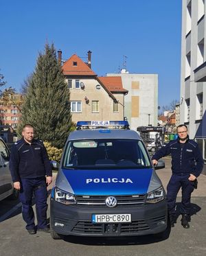 dwaj umundurowani policjanci stojący po obu stronach radiowozu