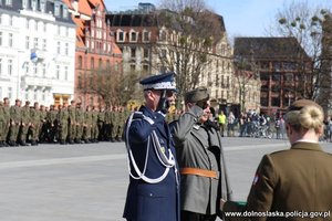 komendant wojewódzki Policji we Wrocławiu stoi na placu z mężczyzną ubranym w stój wojskowy z czasów II wojny światowej, w tle żołnierze podczas uroczystości
