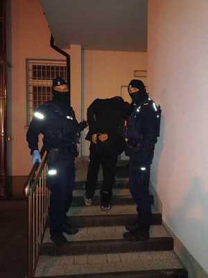 funkcjonariusze na stoją na schodach z zatrzymanym mężczyzną w kajdankach