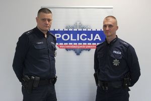 dwaj policjanci na tle baneru z napisem policja