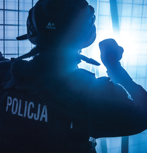 policjant podczas ćwiczeń z PSP, funkcjonariusz na zdjęciu stoi tyłem, w ręku trzyma latarkę