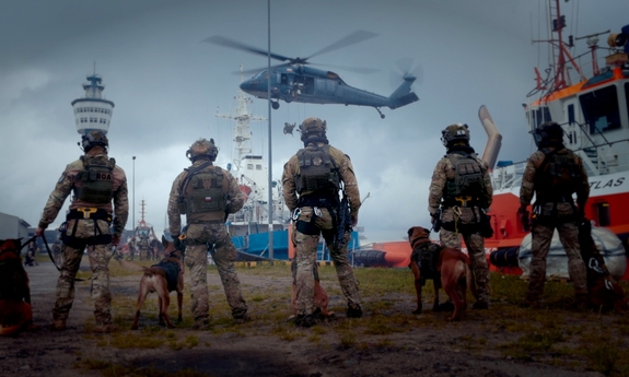 Zntyterroryści z psami obserwują policyjny śmigłowiec.