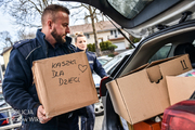 Umundurowany policjant pakuje do bagażnika karton z napisem: książki dla dzieci