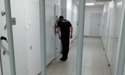Policjant w izbie zatrzymań zagląda do celi przez wizjer. Na pierwszym planie krata aresztu