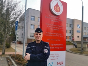 umundurowany policjant stoi przed tablica z napisem: Regionalne Centrum Krwiodawstwa i Krwiolecznictwa w Białymstoku