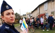 Zdjęcie przedstawia policjantkę stojącą z ulotkami, w tle widać grupę uchodźców z Ukrainy