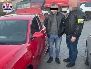 policjant z zatrzymanym mężczyzną w kajdankach stoją przy samochodzie