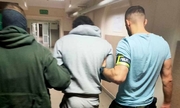 dwaj nieumundurowani policjanci prowadzą korytarzem zatrzymanego mężczyznę