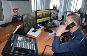 policjant dyżurny rozmawia przez telefon siedząc przy swoim stanowisku służby