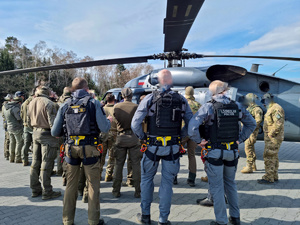 Na tle stojącego bokiem Black Hawka policjanci sfotografowani od tyłu w różnych mundurach taktycznych.