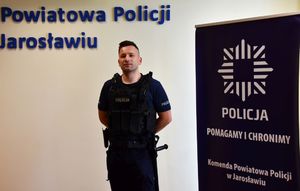 Umundurowany funkcjonariusz — sierż. szt. Daniel Madejowski stoi na tle ściany z napisem Komenda Powiatowa Policji w Jarosławiu