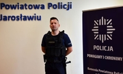 Umundurowany funkcjonariusz — sierż. szt. Daniel Madejowski stoi na tle ściany z napisem Komenda Powiatowa Policji w Jarosławiu