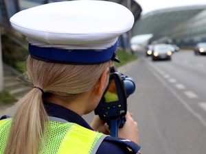 Policjantka z ręcznym miernikiem prędkości kontroluje prędkość poruszających się po drodze pojazdów