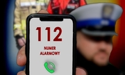 policjant trzyma telefon na którym wyświetla się numer 112 numer alarmowy i zielona słuchawka