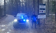 policjant stoi przy samochodzie terenowym na drodze w lesie