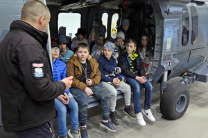 Dzieci siedzą na pokładzie helikoptera, obok stoi pilot i opowiada o maszynie.