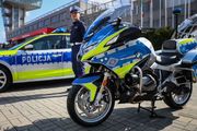 nowo oznakowany radiowóz i motocykl. Między nimi stoi umundurowany policjant ruchu drogowego