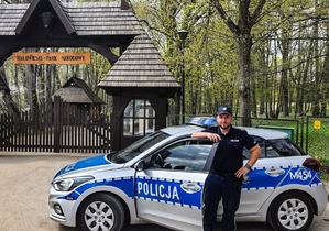 policjant stoi przy radiowozie, w tle Białowieski Park Narodowy