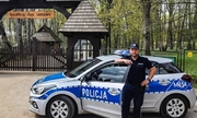 policjant stoi przy radiowozie, w tle Białowieski Park Narodowy